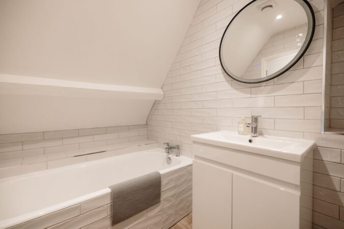 Main family bathroom with full-size bathtub, overhead shower, and modern tiling at The Hideaway